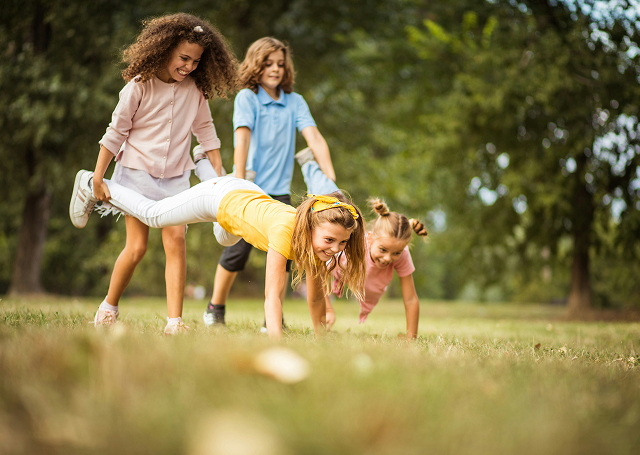 Drei Mädchen spielen Schubkarre im Grünen. Spaß und Bewegung im Freien.